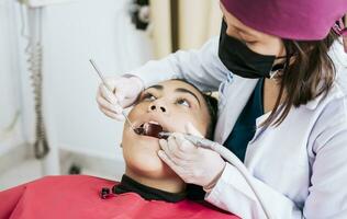 fêmea dentista limpeza e examinando uma fêmea paciente boca. dental especialista limpeza a dentes do uma fêmea paciente. profissional dentista limpeza uma fêmea pacientes boca foto