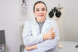 optometria especialista com polegar acima. sorridente olho médico com polegar acima dentro escritório, fêmea optometrista com polegar acima dentro a laboratório foto