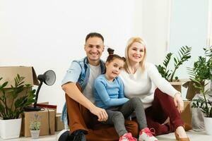 feliz família sentado em de madeira chão. pai, mãe e criança tendo Diversão junto. comovente casa dia, Novo casa e Projeto interior conceito foto