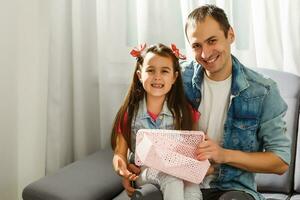 sorridente filha dando presente para pai enquanto sentado em sofá às casa foto