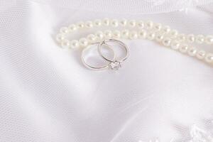 uma par do branco ouro noivado argolas com uma diamante em a a branco véu do a noiva e pérola miçangas. disposição para a convite, cobrir. foto