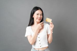 mulher asiática com cara feliz e apresentando cartão de crédito na mão, mostrando confiança e segurança para fazer o pagamento foto