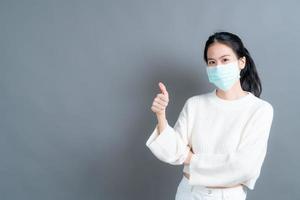 jovem mulher asiática usando máscara médica e fazendo sinal de positivo