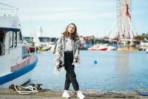 lindo menina em pé perto iate em cais. Porto Maritimo ou atracar dentro fundo. jovem mulher vestindo casual equipamento posando perto água dentro ensolarado dia. pessoas estilo de vida e descansar conceito. borrado fundo foto