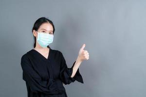 jovem mulher asiática usando máscara médica e fazendo sinal de positivo