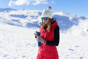 feliz mulher em pé com água garrafa dentro luz solar em Nevado terreno foto