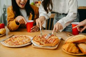 grupo do amigos fazer Diversão às casa festa.eles sentado em escrivaninha dentro vivo quarto e comendo pizza. foto