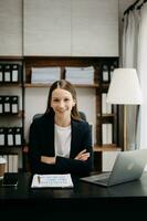 confiante o negócio especialista atraente sorridente jovem mulher digitando computador portátil ang segurando digital tábua em escrivaninha dentro escritório. foto