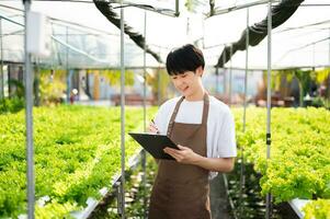 ásia casal do agricultores inspeciona plantas com uma digital tábua dentro uma estufa plantação. inteligente agricultura foto