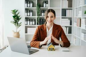 agente imobiliário feminino usa as mãos para proteger o telhado vermelho para o conceito de investimento imobiliário sobre comércio de casas, compra na mesa do escritório foto