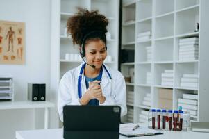 atraente africano fêmea médico falando enquanto explicando médico tratamento para paciente através uma vídeo ligar com computador portátil dentro escritório ou laboratório foto