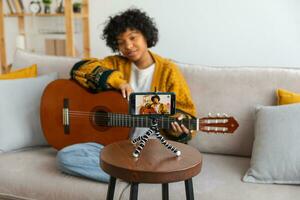 blogueiro guitarrista. africano americano menina blogueiro jogando guitarra falando para Webcam gravação vlog. social meios de comunicação influenciador mulher transmissão às casa dentro de casa. música conteúdo O Criador transmissão tutorial. foto