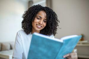 jovem lindo africano americano mulher segurando livro, universidade aluna estudo, Aprendendo linguagem. lazer, literatura e pessoas conceito - sorridente africano americano mulher lendo livro às casa foto