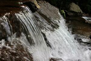 fechar-se Visão do Claro água em cascata baixa rio pedras foto