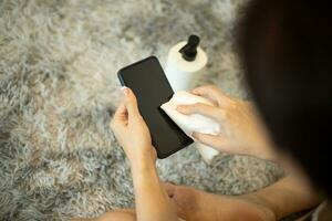 mãos de mulher limpando a tela do telefone com álcool em casa foto