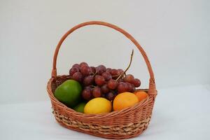 frutas dentro uma cesta em uma branco fundo. laranja, uva, limão. foto