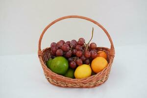 frutas dentro uma cesta em uma branco fundo. laranja, uva, limão. foto