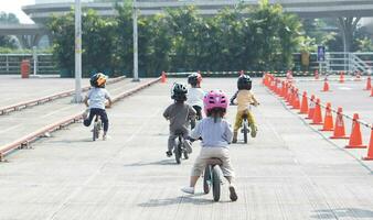 crianças a partir de 2-5 anos velho raças em Saldo bicicleta dentro uma estacionamento área com cones Como acompanhar, costas visualizar, atrás Visão atirar. foto