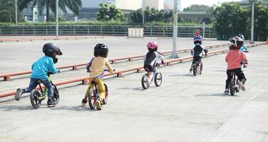 crianças a partir de 2-5 anos velho raças em Saldo bicicleta dentro uma estacionamento área, costas visualizar, atrás Visão atirar. foto