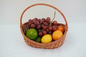 frutas dentro uma cesta em uma branco fundo. laranja, uva, limão. foto