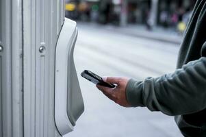 homem usando Smartphone toque para pagar às pagar estação para bilhete ou transporte Serviços, Comprar e Varredura para pagar foto