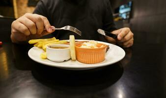 homem comendo grelhado carnes estaca a partir de placa. mão segurando faca e garfo corte grelhado carne bife foto