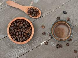 topo Visão do Preto espresso café dentro uma vidro copo com café feijões em uma de madeira mesa foto