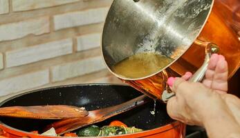 chefe de cozinha é derramando frango caldo a partir de cobre Panela para dentro cozinhando prato com ingredientes foto