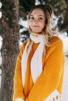 adolescente Loiras dentro uma amarelo suéter lado de fora dentro inverno. uma Adolescência menina em uma andar dentro inverno roupas dentro uma Nevado floresta foto