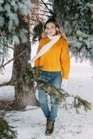 adolescente Loiras dentro uma amarelo suéter lado de fora dentro inverno. uma Adolescência menina em uma andar dentro inverno roupas dentro uma Nevado floresta foto