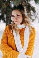 adolescente Loiras dentro uma amarelo suéter lado de fora dentro inverno. uma Adolescência menina em uma andar dentro inverno roupas dentro uma Nevado floresta foto