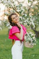 feliz para uma jovem lindo mulher dentro uma Primavera jardim segurando uma cesta do flores e sorridente foto
