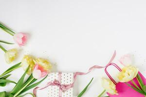 lindo Primavera Rosa e amarelo tulipas flores com branco fita com brilhante saco em branco. plano deitar. cópia de espaço. mulher dia ou dia dos namorados dia presente. conceito do feriado Primavera venda dentro loja foto