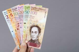 venezuelano dinheiro dentro a mão em uma cinzento fundo foto