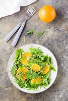 dieta vegetariano Vitamina salada do laranja peças e misturar do Rúcula, acelga e mizun folhas em uma prato em a mesa. topo e vertical Visão foto