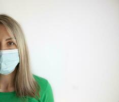 retrato do uma jovem mulher dentro uma médico mascarar isolado sobre cinzento fundo. jovem menina paciente carrinhos contra a parede fundo, cópia de espaço para texto. foto