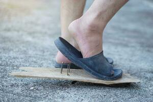 fechar-se homem vestem sapatos é pisar em oxidado metal unha em madeira. conceito, inseguro , risco para perigoso tétano. estar Cuidado e Veja por aí durante caminhando em a chão ou risco lugares. acidente foto