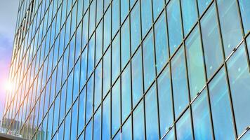 estrutural vidro parede refletindo azul céu. abstrato moderno arquitetura fragmento. vidro construção com transparente fachada do a construção e azul céu. contemporâneo arquitetônico fundo. foto
