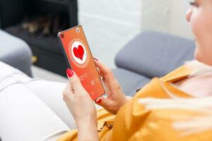 mulher sentado em a sofá e segurando uma telefone com aplicativo para saúde cartão monitoramento foto