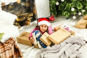 retrato do bonita pequeno menina perto uma lareira dentro Natal foto