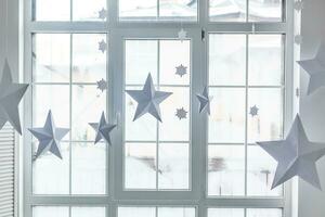 grande janela brilhante. no parapeito da janela há um xadrez de malha cinza com presentes e brilhos com suas terras. estrelas de natal de papel estão suspensas no fundo da janela. foto