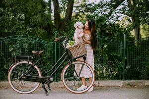 jovem colocando cachorro bichon frise branco na cesta da bicicleta elétrica foto