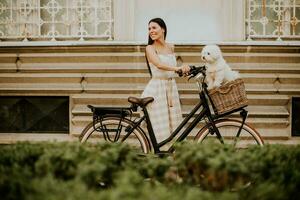 jovem mulher com cachorro branco bichon frise na cesta de bicicleta elétrica foto