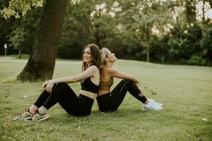 dois bonita jovem mulheres sentado em Relva e relaxante depois de ao ar livre Treinamento foto