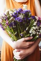 menina segurando uma ramalhete do limonium sinuatum ou statice flores dentro dela mãos. variedade do colorida limonium sinuatum ou statice Salem flores - branco, amarelo, rosa, roxo, tolet e azul foto