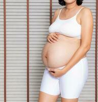retrato do uma grávida mulher tocante dela grande barriga fechar acima, mãe, gravidez, pessoas e expectativa. mulher segurando grande grávida estômago foto