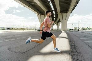 uma desportivo masculino atleta Treinamento faz aquecer exercícios. corrida dentro a tarde dentro a cidade. corredor treinador dentro ginástica roupas camiseta. usa uma ginástica assistir. foto