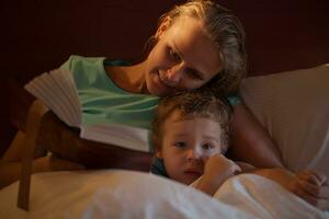 mãe lendo uma hora de dormir história para dela pequeno filho foto