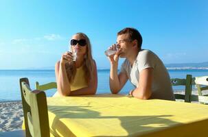 jovem casal desfrutando bebidas às a beira-mar foto