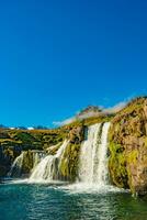 Maravilhoso cascata nomeado Kirkjufellsfoss com uma kirkjufell Igreja gostar icônico montar dentro ocidental Islândia, às azul céu e ensolarado dia foto